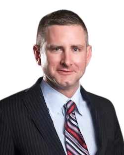 man in a dark pinstripe suit, light blue shirt, and striped tie, with short brown hair, posing against a plain white background.